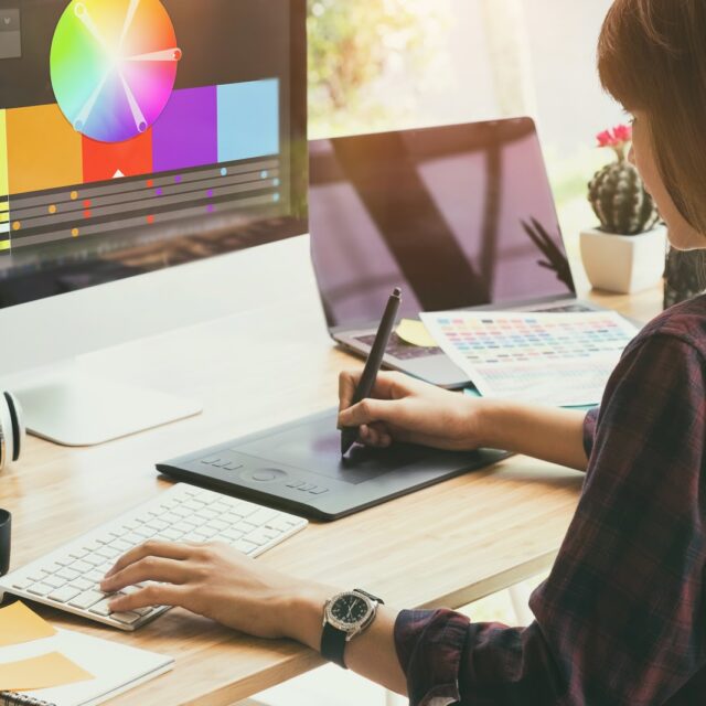 Graphic designer working on creative desk computer while using graphic tablet at desk in the office